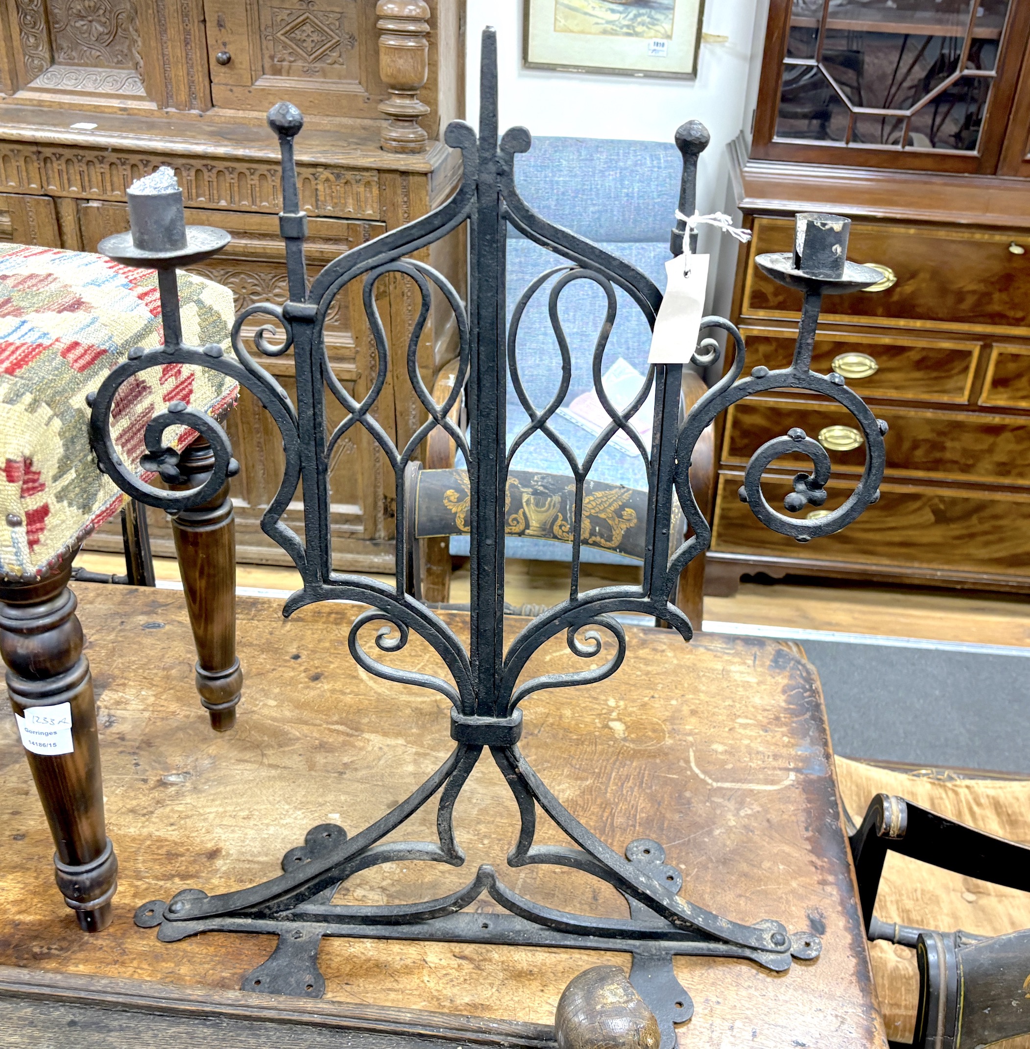 A pair of Gothic wrought iron three light candelabra, width 46cm, height 76cm, Provenance- Brede Place chapel, East Sussex, a former residence of the Frewen family from 1712-1936.
